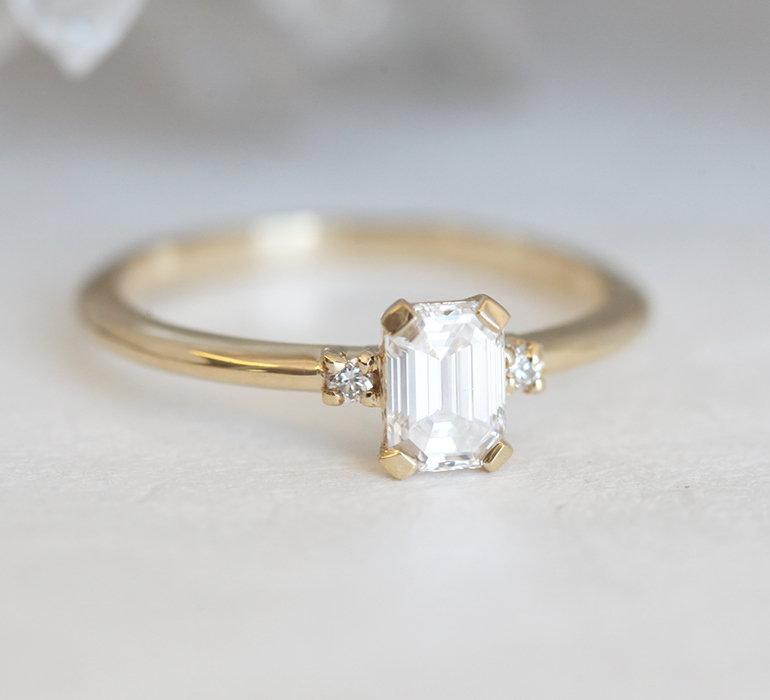 Smaragdno brušeni dijamantski prsten sa bočnim dijamantima od 14k žutog zlata, koji pokazuje eleganciju i sjaj.