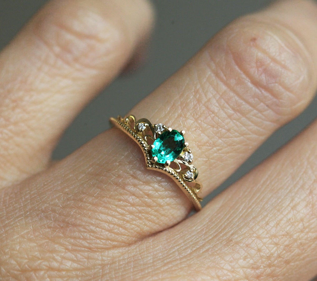 Elegantan ovalni smaragdni prsten sa smaragdnim klasterom markiznog reza i dijamantima. Bend u vintage stilu od 14k ili 18k zlata.