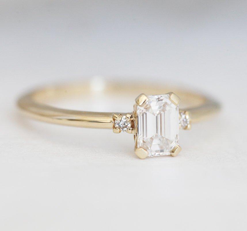 Smaragdno brušeni dijamantski prsten sa bočnim dijamantima, koji pokazuje elegantnu jednostavnost i sjaj. Spremni za isporuku od 14k žutog zlata.